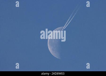 Ein Passagierflugzeug fährt in einer Höhe von 40,000 Metern und passiert vor dem Halbmond an einem wolkenlosen sonnigen Frühlingstag, während das Flugzeug über Europa am niederländischen Himmel fliegt. Moonpass ist das ultimative Ziel der Luftfahrtfotografen, der Planespotter. Während des Fluges hinterlässt der Passagierjet Kondensstreifen oder Kondensstreifen, eine weiße Dampflinie, während er vor dem natürlichen Satelliten der Erde und dem nächsten Himmelsoobjekt im Universum vorbeiläuft. Eindhoven, Niederlande, am 24. April 2022. (Foto von Nicolas Economou/NurPhoto) Stockfoto