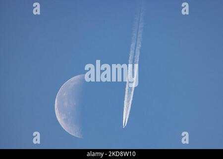 Ein Passagierflugzeug fährt in einer Höhe von 40,000 Metern und passiert vor dem Halbmond an einem wolkenlosen sonnigen Frühlingstag, während das Flugzeug über Europa am niederländischen Himmel fliegt. Moonpass ist das ultimative Ziel der Luftfahrtfotografen, der Planespotter. Während des Fluges hinterlässt der Passagierjet Kondensstreifen oder Kondensstreifen, eine weiße Dampflinie, während er vor dem natürlichen Satelliten der Erde und dem nächsten Himmelsoobjekt im Universum vorbeiläuft. Eindhoven, Niederlande, am 24. April 2022. (Foto von Nicolas Economou/NurPhoto) Stockfoto