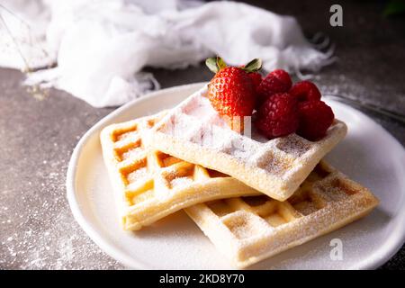 Frische hausgemachte, weiche Waffeln mit Obst und Puderzucker auf weißem Teller serviert. Stockfoto