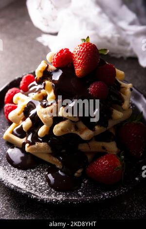 Frische hausgemachte, weiche Waffeln mit Obst und Puderzucker, bedeckt mit viel geschmolzener Schokolade. Stockfoto