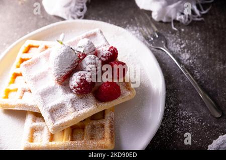 Frische hausgemachte, weiche Waffeln mit Obst und Puderzucker auf weißem Teller serviert. Stockfoto