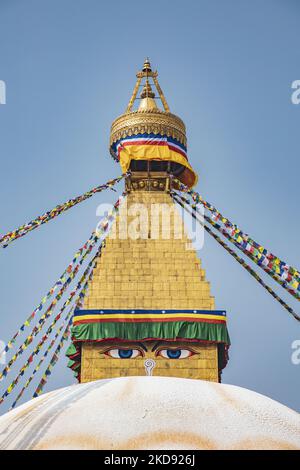 Nahaufnahme an der goldenen Spitze mit den Augen der Stupa, wo die Gebetsfahnen beginnen. Boudhanath oder Bouddha Stupa in Kathmandu ein UNESCO-Weltkulturerbe und ein legendärer Ort für die newarische und tibetisch-buddhistische Mythologie mit dem goldenen Teil, der die Augen von Boudhanath und die Gebetsfahnen hat. Das Mandala, eine der beliebtesten Touristenattraktionen in Kathmandu, macht es zu einem der größten kugelförmigen Stupas in Nepal und der Welt. Die Stupa wurde beim Erdbeben vom 2015. April beschädigt. Die Stupa befindet sich auf der alten Handelsstraße von Tibet, und die tibetischen Flüchtlinge nach dem 1950s beschlossen, Li Stockfoto