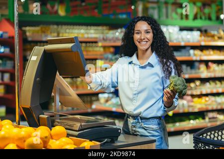 Porträt einer glücklichen Shopper in einem Supermarkt in der Obst- und Gemüseabteilung, hispanic Frau wiegen Kohl lächelnd und Blick auf die Kamera. Stockfoto