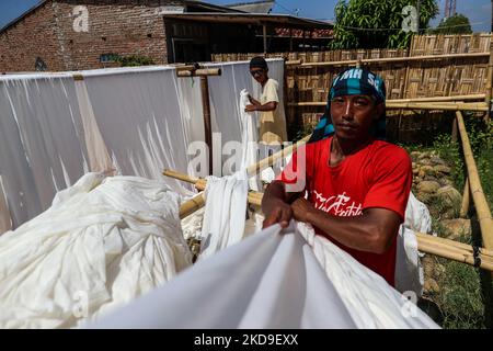 Arbeiter hängen ein Tuch, um in der Sonne an Häusern im niedrig gelegenen Jeruk Sari-Viertel an der Küste von Pekalongan, Zentraljava, Indonesien, zu trocknen, 5. Juni 2021. Ein Gebiet, in dem fast jeder verfügbare Raum für die Batikproduktion genutzt wird, mit einem hohen Armutsniveau, das sowohl durch den steigenden Meeresspiegel als auch durch hohe Flussspitzenströme gefährdet ist. Sie hängen und waschen an einem verschmutzten Fluss, um traditionelles javanesisches Textil namens Batik zu verarbeiten. Batik ist eine traditionelle indonesische Methode zur Verwendung von Wachs, um wasserbasierten Farbstoffen zu widerstehen, um Muster und Zeichnungen auf Stoff darzustellen. Im Mittelpunkt des PR Stockfoto