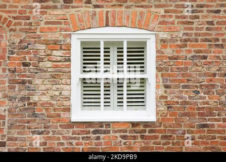 Außenansicht eines alten Backsteinhauses mit Holzfenster und Holzjalousien, England, Großbritannien Stockfoto