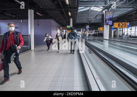 Passagiere, die Gesichtsmasken im Terminal, in der Abflughalle und im Abflugbereich des Flughafens Amsterdam Schiphol tragen, sehen AMS EHAM vor ihrem Abflug aufgrund von Covid-19-Pandemiemaßnahmen, während auf Transparenten im Flughafen die Verwendung der Maske angezeigt wird. Ab dem 16. Mai 2022 werden für den Flugverkehr in Europa keine Gesichtsmasken mehr benötigt, wie die Europäische Agentur für Flugsicherheit EASA und das Europäische Zentrum für die Prävention und die Kontrolle von Krankheiten ECDC angekündigt haben. Die Regel einer obligatorischen Gesichtsmask im Flugzeug ist in einigen Ländern bereits beendet, da viele die Maßnahmen und Beschränkungen aussetzen, um die SP zu verhindern Stockfoto