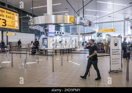 Passagiere, die Gesichtsmasken im Terminal, in der Abflughalle und im Abflugbereich des Flughafens Amsterdam Schiphol tragen, sehen AMS EHAM vor ihrem Abflug aufgrund von Covid-19-Pandemiemaßnahmen, während auf Transparenten im Flughafen die Verwendung der Maske angezeigt wird. Ab dem 16. Mai 2022 werden für den Flugverkehr in Europa keine Gesichtsmasken mehr benötigt, wie die Europäische Agentur für Flugsicherheit EASA und das Europäische Zentrum für die Prävention und die Kontrolle von Krankheiten ECDC angekündigt haben. Die Regel einer obligatorischen Gesichtsmask im Flugzeug ist in einigen Ländern bereits beendet, da viele die Maßnahmen und Beschränkungen aussetzen, um die SP zu verhindern Stockfoto