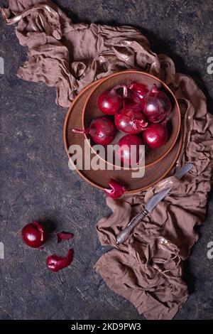 Reife rote Zwiebelbirnen in einer Tonschale auf einer Steinoberfläche, flach liegend, Low-Key-Fotografie mit freiem Platz für Text Stockfoto