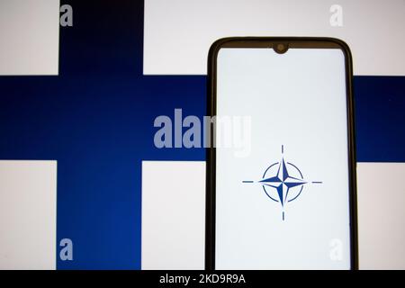 Auf dieser Abbildung ist eine Flagge der NATO zu sehen, die auf einem Smartphone-Bildschirm mit der Flagge Finnlands im Hintergrund in Athen, Griechenland, am 12. Mai 2022 angezeigt wird. Finnland und Schweden beantragten den Beitritt zur NATO. (Foto-Illustration von Nikolas Kokovlis/NurPhoto) Stockfoto