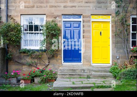 Blau und gelb gestrichene Eingangstüren an Reihenhäusern. Ferienhäuser, Robin Hoods Bay, Yorkshire, Großbritannien Stockfoto