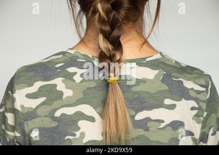 Mädchen in einer militärischen grünen Tarnuniform mit einer Sense auf einem isolierten Hintergrund, Rückansicht, Soldatin Stockfoto