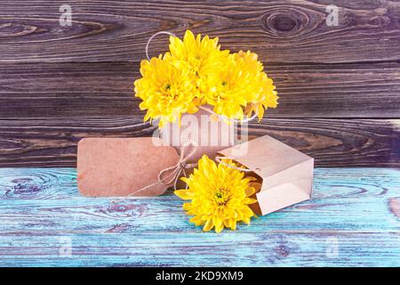 Gelbe Blüten einer Chrysantheme mit Geschenken und Platz für Grußtext, selektiver Fokus. Stillleben auf einem hölzernen Hintergrund Stockfoto