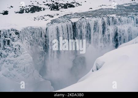 Eine Luftaufnahme des fließenden Wasserfalls von Felsen umgeben von schneebedeckten Feld Stockfoto