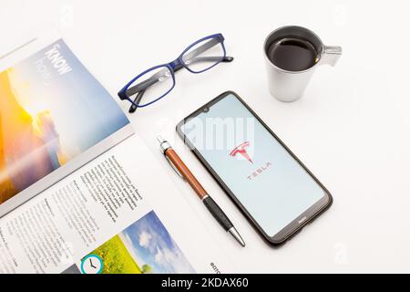 In dieser Fototafel wurde am 25. Mai 2022 ein Tesla Motors-Logo auf einem Smartphone-Bildschirm auf einem Schreibtisch neben einem Café, einem Stift, einer Brille und einer Zeitschrift in Athen, Griechenland, abgebildet. (Foto-Illustration von Nikolas Kokovlis/NurPhoto) Stockfoto