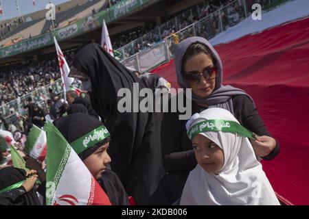 Eine Frau hilft ihrer jungen Tochter, ein Stirnband zu tragen, während sie am 26. Mai 2022 an einer Versammlung zur Hymne „Hello Commander“ im Azadi-Fußballstadion mit hunderttausend Sitzplätzen im Westen von Teheran zur Unterstützung des iranischen Obersten Führers Ayatollah Ali Khamenei teilnahm. Hunderttausend Anhänger des iranischen Obersten Führers Ayatollah Ali Khamenei versammelten sich im Sportkomplex Azadi (Freiheit), um den Hymnus Hallo Kommandant zu singen. (Foto von Morteza Nikoubazl/NurPhoto) Stockfoto