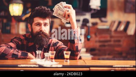 Hipster hält Geld und zählt Bargeld, um mehr Alkohol zu kaufen. Stockfoto