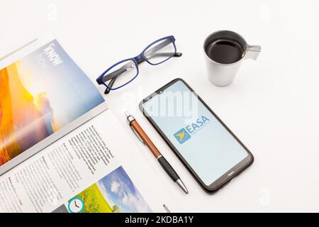 In dieser Abbildung ist ein Logo der Europäischen Agentur für Flugsicherheit (EASA) zu sehen, das am 31. Mai 2022 auf einem Smartphone-Bildschirm auf einem Schreibtisch neben einem Café, einem Stift, einer Brille und einer Zeitschrift in Athen, Griechenland, zu sehen ist. (Foto-Illustration von Nikolas Kokovlis/NurPhoto) Stockfoto