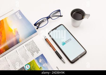 In dieser Abbildung ist ein Logo von Molina Healthcare zu sehen, das am 5. Juni 2022 auf einem Smartphone-Bildschirm auf einem Schreibtisch neben einem Café, einem Stift, einer Brille und einem Magazin in Athen, Griechenland, abgebildet ist. (Fotoillustration von Nikolas Kokovlis/NurPhoto) Stockfoto
