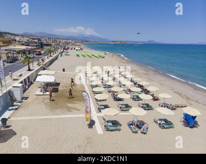Luftaufnahmen von einer Drohne der Küste der Stadt Rethymno mit dem langen Strand und den Strandbars auf der Insel Creta. Man sieht die Menschen an der Strandbar unter dem Sonnenschirm die Sonne genießen oder im kristallklaren Meer schwimmen. Rethymno ist eine historische mediterrane Strandstadt an der Nordküste Kretas, die an der Ägäis liegt und 40,000 Einwohner zählt. Ein touristisches Ziel mit einem historischen venezianischen Hafen und einer Stadt, archäologischen Stätten, endlosen Sandstränden, Wassersportmöglichkeiten, schönen, traditionellen Tavernen und einer großen Auswahl an Hotels. Der Tourismus kehrt zurück, und die Vorbehalte steigen Stockfoto