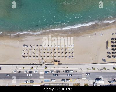 Luftaufnahmen von einer Drohne der Küste der Stadt Rethymno mit dem langen Strand und den Strandbars auf der Insel Creta. Man sieht die Menschen an der Strandbar unter dem Sonnenschirm die Sonne genießen oder im kristallklaren Meer schwimmen. Rethymno ist eine historische mediterrane Strandstadt an der Nordküste Kretas, die an der Ägäis liegt und 40,000 Einwohner zählt. Ein touristisches Ziel mit einem historischen venezianischen Hafen und einer Stadt, archäologischen Stätten, endlosen Sandstränden, Wassersportmöglichkeiten, schönen, traditionellen Tavernen und einer großen Auswahl an Hotels. Der Tourismus kehrt zurück, und die Vorbehalte steigen Stockfoto