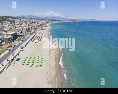 Luftaufnahmen von einer Drohne der Küste der Stadt Rethymno mit dem langen Strand und den Strandbars auf der Insel Creta. Man sieht die Menschen an der Strandbar unter dem Sonnenschirm die Sonne genießen oder im kristallklaren Meer schwimmen. Rethymno ist eine historische mediterrane Strandstadt an der Nordküste Kretas, die an der Ägäis liegt und 40,000 Einwohner zählt. Ein touristisches Ziel mit einem historischen venezianischen Hafen und einer Stadt, archäologischen Stätten, endlosen Sandstränden, Wassersportmöglichkeiten, schönen, traditionellen Tavernen und einer großen Auswahl an Hotels. Der Tourismus kehrt zurück, und die Vorbehalte steigen Stockfoto