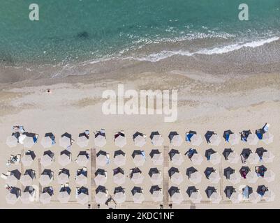 Luftaufnahmen von einer Drohne der Küste der Stadt Rethymno mit dem langen Strand und den Strandbars auf der Insel Creta. Man sieht die Menschen an der Strandbar unter dem Sonnenschirm die Sonne genießen oder im kristallklaren Meer schwimmen. Rethymno ist eine historische mediterrane Strandstadt an der Nordküste Kretas, die an der Ägäis liegt und 40,000 Einwohner zählt. Ein touristisches Ziel mit einem historischen venezianischen Hafen und einer Stadt, archäologischen Stätten, endlosen Sandstränden, Wassersportmöglichkeiten, schönen, traditionellen Tavernen und einer großen Auswahl an Hotels. Der Tourismus kehrt zurück, und die Vorbehalte steigen Stockfoto