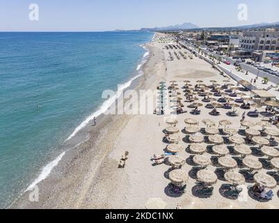Luftaufnahmen von einer Drohne der Küste der Stadt Rethymno mit dem langen Strand und den Strandbars auf der Insel Creta. Man sieht die Menschen an der Strandbar unter dem Sonnenschirm die Sonne genießen oder im kristallklaren Meer schwimmen. Rethymno ist eine historische mediterrane Strandstadt an der Nordküste Kretas, die an der Ägäis liegt und 40,000 Einwohner zählt. Ein touristisches Ziel mit einem historischen venezianischen Hafen und einer Stadt, archäologischen Stätten, endlosen Sandstränden, Wassersportmöglichkeiten, schönen, traditionellen Tavernen und einer großen Auswahl an Hotels. Der Tourismus kehrt zurück, und die Vorbehalte steigen Stockfoto