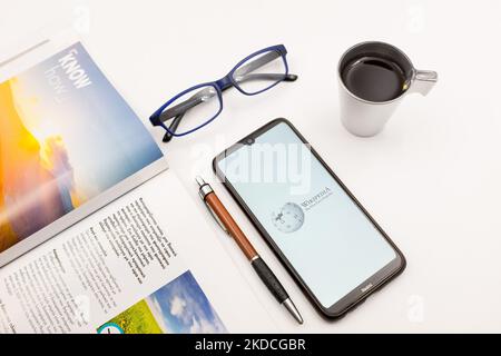 In dieser Fototafel wurde ein Wikipedia-Logo auf einem Smartphone-Bildschirm auf einem Schreibtisch neben einem Café, einem Stift, einer Brille und einer Zeitschrift am 22. Juni 2022 in Athen, Griechenland, angezeigt. (Foto von Nikolas Kokovlis/NurPhoto) Stockfoto