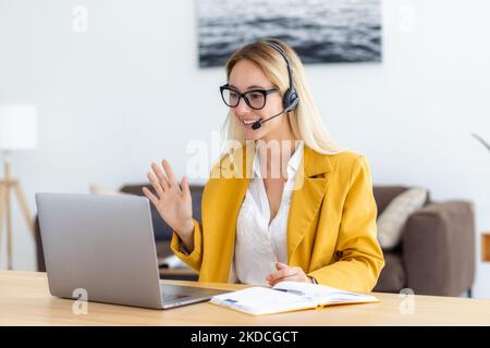 Eine junge Frau im Headset, die in einem Videomeeting mit Mitarbeitern oder dem Kunden online über einen Laptop kommuniziert Stockfoto