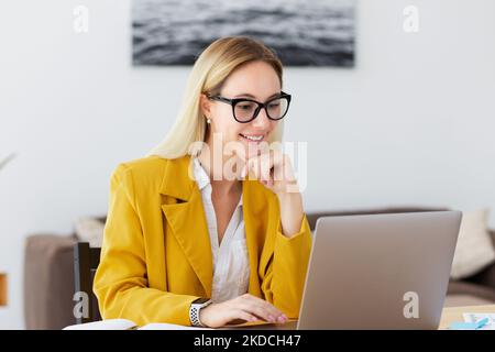 Schöne junge Frau arbeitet mit Computer-Laptop konzentriert und lächelnd, Online-Fernarbeit, lächelnd Stockfoto