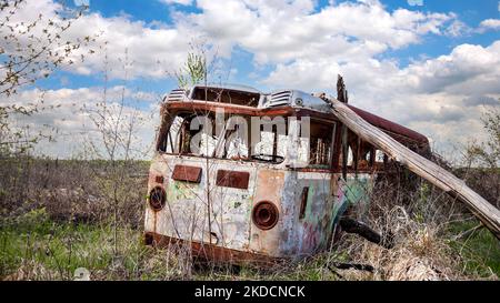 Ein verlassene alte Bus sitzt rostend im Unkraut eines ländlichen Feldes unter einem bewölkten Himmel Stockfoto