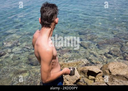 Am 30. Juni 2022 fängt ein Mann am Strand von Skliri auf der griechischen Insel Aigina lila Quallen mit einer türkischen Kaffeekocher. Viele Quallen erschienen an den Stränden aufgrund der starken Winde in Griechenland. (Foto von Nikolas Kokovlis/NurPhoto) Stockfoto