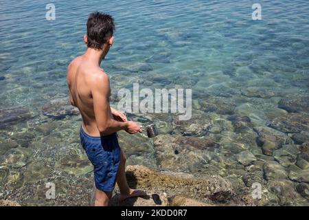 Am 30. Juni 2022 fängt ein Mann am Strand von Skliri auf der griechischen Insel Aigina lila Quallen mit einer türkischen Kaffeekocher. Viele Quallen erschienen an den Stränden aufgrund der starken Winde in Griechenland. (Foto von Nikolas Kokovlis/NurPhoto) Stockfoto