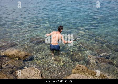 Am 30. Juni 2022 fängt ein Mann am Strand von Skliri auf der griechischen Insel Aigina lila Quallen mit einer türkischen Kaffeekocher. Viele Quallen erschienen an den Stränden aufgrund der starken Winde in Griechenland. (Foto von Nikolas Kokovlis/NurPhoto) Stockfoto