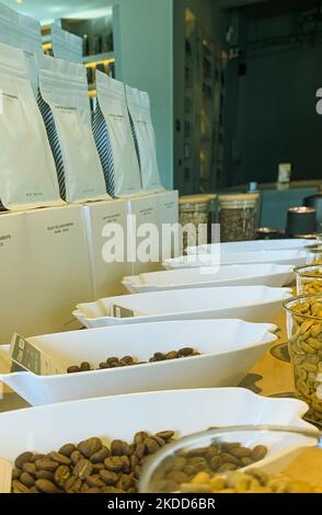 Eine vertikale Nahaufnahme der Innenseite eines Coffee Shops mit Kaffeebohnen auf einer weißen Schüssel und ordentlich angeordneten Glasbechern Stockfoto