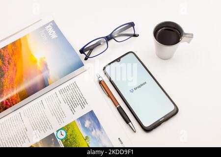 In dieser Abbildung ist ein Dropbox-Logo zu sehen, das am 7. Juli 2022 auf einem Smartphone-Bildschirm auf einem Schreibtisch neben einem Café, einem Stift, einer Brille und einem Magazin in Athen, Griechenland, zu sehen ist. (Foto-Illustration von Nikolas Kokovlis/NurPhoto) Stockfoto