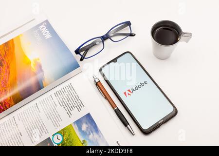 In dieser Fototafel wurde ein Adobe-Logo auf einem Smartphone-Bildschirm auf einem Schreibtisch neben einem Café, einem Stift, einer Brille und einer Zeitschrift am 7. Juli 2022 in Athen, Griechenland, angezeigt. (Foto-Illustration von Nikolas Kokovlis/NurPhoto) Stockfoto