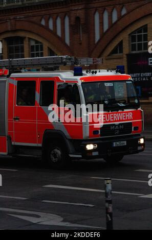 Nahaufnahme eines orangefarbenen Feuerwehrautos auf der Berliner Straße mit Feuerwehrleuten und einem Backsteingebäude im Hintergrund Stockfoto