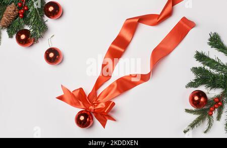 weihnachtsdekorationen auf weißem Hintergrund mit orangefarbenem Band und roten Baknotn-Kugeln in der Draufsicht ist von oben Stockfoto