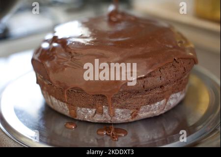 Frisch gegossenes Schokoladenicing, das einen hausgebackenen Kuchen auf einem Metalltablett in Nahsicht abtropft Stockfoto