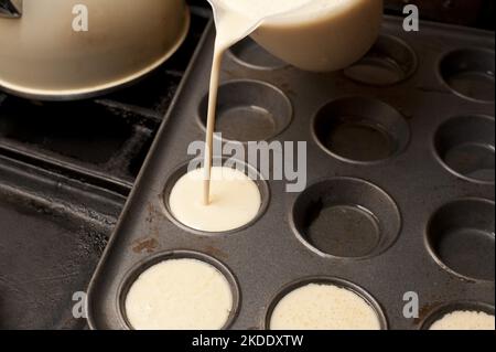 Kochen Sie das Gießen von frisch zubereitetem Teig aus einem Krug in ein Backblech mit individuellen Becherhaltern für eine Partie englischer Yorkshire Puddings Stockfoto