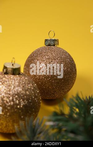 goldene Weihnachtskugeln auf gelbem Hintergrund mit grüner Kiefer Stockfoto