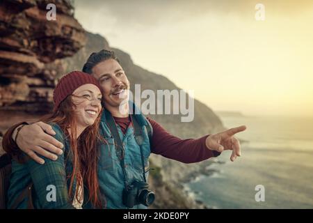 Jetzt gibt es etwas zu sehen. Ein liebevolles junges Paar, das den Blick von einem Berggipfel aus betrachtet. Stockfoto