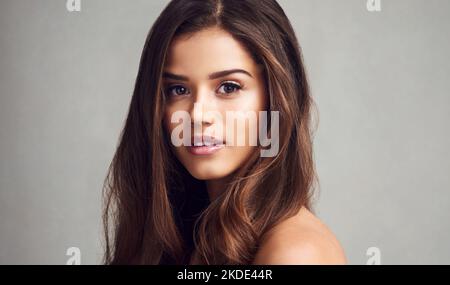 Brünett und schön. Studioaufnahme einer jungen schönen Frau mit langen wunderschönen Haaren, die vor einem grauen Hintergrund posiert. Stockfoto