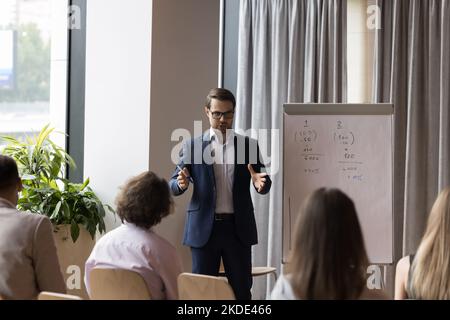 Ein selbstbewusster männlicher Vortragender gibt den Mitarbeitern des Unternehmens eine Unternehmenspräsentation Stockfoto