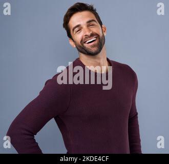 Eine positive Haltung im Leben einnehmen. Studioaufnahme eines hübschen und glücklichen jungen Mannes, der vor grauem Hintergrund posiert. Stockfoto