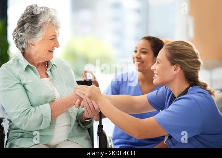 Zwei attraktive Krankenschwestern, die im Krankenhaus mit ihrem Rollstuhl gebundenen Seniorenkrankten sprachen, widmeten sich Ihrer Gesundheit. Stockfoto