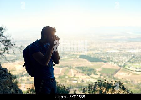 Das Wunder der Welt festhalten. Rückansicht eines jungen Mannes, der ein Foto der malerischen Aussicht von der Spitze eines Berges gemacht hat. Stockfoto