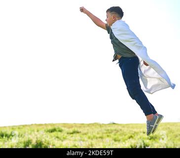 Ein süßer kleiner Junge, der einen Superhelden mit einem Umhang auf der Außenseite spielt. Stockfoto