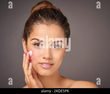 Diese Formel geht direkt an die Arbeit. Porträt eines jungen Models, das im Studio Feuchtigkeitscreme auf ihr Gesicht anwendet. Stockfoto